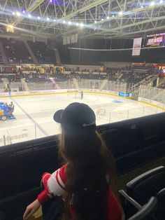 a woman sitting in front of an ice hockey rink watching a game on the ice