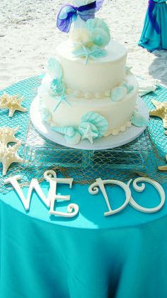 a white and blue wedding cake sitting on top of a table next to the ocean