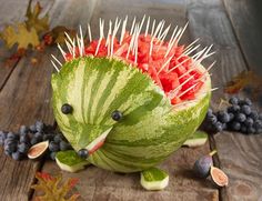 a watermelon sculpture with spikes on it's head and fruit in the background