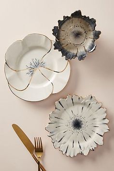 three plates and two forks on a pink surface with gold rimmed utensils