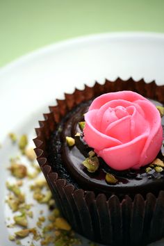 a chocolate cupcake with pink frosting and sprinkles on a white plate