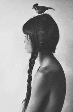 black and white photograph of woman with bird perched on her head, back to camera