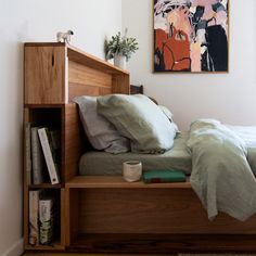 a bed with green sheets and pillows in a small room next to a book shelf