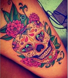 a woman's thigh with a colorful sugar skull and flowers tattoo on her leg