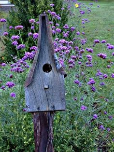 a wooden bird house sitting on top of a tree stump in a garden filled with purple flowers