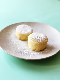 two powdered sugar cookies on a white plate sitting on a blue tablecloth with green background