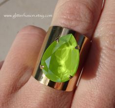 This big statement ring features a genuine Swarovski crystal in the brand new shade Lime. This crystal's bright green color is intensified by a radiant surface shine and is part of the Lacquer Pro series. This teardrop crystal measures 18x13mm. It has been hand set into a shiny gold plated 4 prong wide band setting. The ring band has a split shank in the back, allowing this ring to be gently adjusted to accommodate a variety of sizes. This ring is *best* suited for sizes 6 and up.  This ring wou Wide Gold Ring, Big Statement Rings, Gold Ring Band, Swarovski Crystal Jewelry, Gold Band Ring, Wide Band Rings, Split Shank, Ring Fit, Ring Band