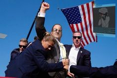 two men shaking hands with an american flag on the back of a truck in front of them