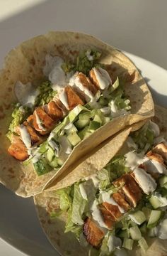 two tacos with chicken and lettuce are on a white plate next to a fork