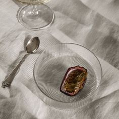 a glass bowl filled with food next to a wine glass and spoon on top of a white table cloth