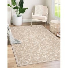 a beige rug with an ornate design on the floor in front of a chair and potted plant