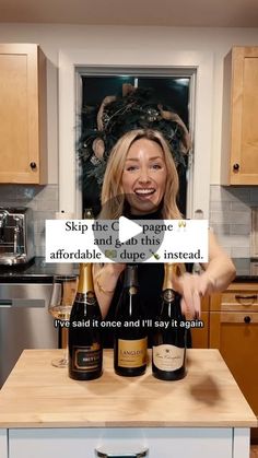 a woman standing in a kitchen with three bottles of wine on top of a counter