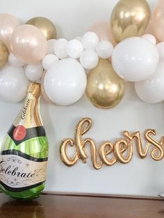 there is a bottle of champagne next to some balloons and a balloon arch with the word cheers on it