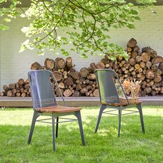 two chairs sitting next to each other on top of green grass near a pile of logs