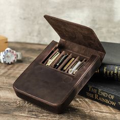 an open leather book case sitting on top of a wooden table next to two books