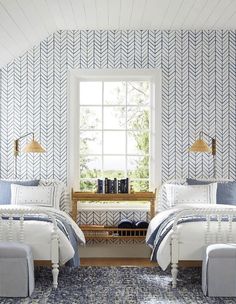 two beds sitting next to each other in a room with blue and white wallpaper