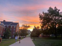 two people walking down a sidewalk in front of a building at sunset with the sun going down