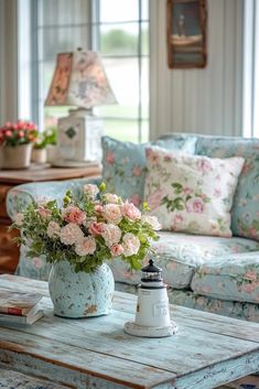 a blue vase with pink flowers sitting on top of a table in front of a couch