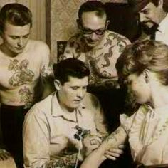 a group of men and women with tattoos on their bodies sitting at a table together