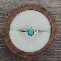 a ring with a turquoise tear sits in a wooden box