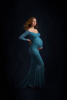 a pregnant woman in a blue gown poses for a photo with her hands on her hips