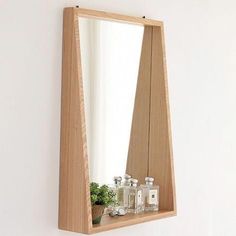 a wooden mirror hanging on the wall next to a shelf with bottles and plants in it