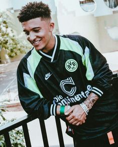 a young man standing on top of a balcony next to a fence and smiling at the camera