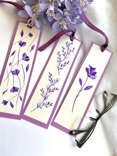 three bookmarks with purple flowers on them next to some scissors and lavender flowers in the background