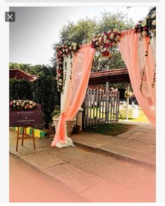 an outdoor wedding setup with pink drapes and flowers on the arch, in front of a wooden bench