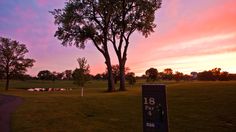 the sun is setting over a golf course with trees in the foreground and water on the far side