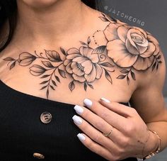 a woman wearing a black top with flowers on her chest and white nails holding onto her hand