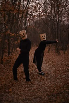 two people with paper bags on their heads are walking through the woods in halloween costumes