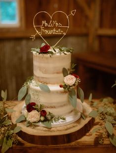 a three tiered cake with flowers and greenery on the top is sitting on a wooden table