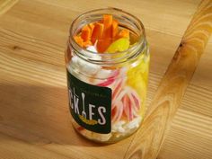 a jar filled with pickles and carrots on top of a wooden table next to a knife