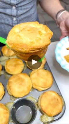 a person holding a spoon over a muffin tin filled with pies on top of a pan