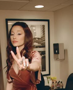 a woman in a brown dress making the v sign with her hand while standing next to a desk