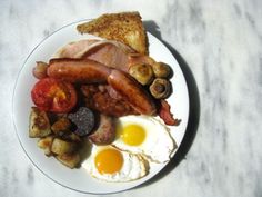 a white plate topped with bacon, eggs and sausage next to toast on a table