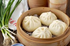 three dumplings are in a bamboo basket next to some green onions