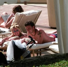 a man and woman laying on lounge chairs next to each other in the sun with their arms around each other