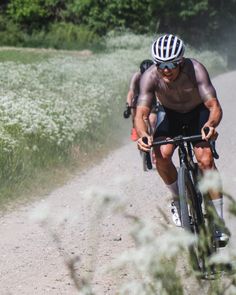 a man riding a bike down a dirt road next to tall grass and trees in the background