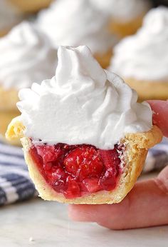 a hand holding a strawberry shortcake with whipped cream on top and another cupcake in the background