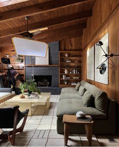 a living room filled with furniture and a fire place in the middle of a wood paneled wall