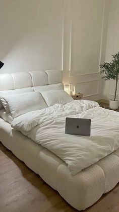 a laptop computer sitting on top of a bed in a room with white sheets and pillows