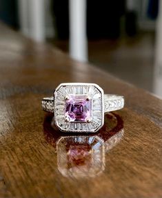 an engagement ring with a pink sapphire surrounded by diamonds on a wooden table in front of a doorway