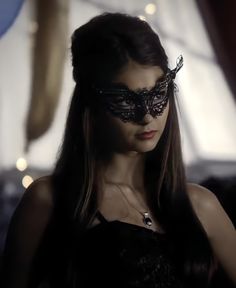 a woman wearing a black masquerade in front of a window with lights behind her