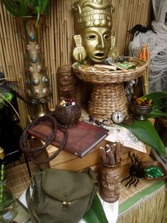 a table topped with lots of assorted items next to a bamboo mask and plant