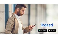 a man looking at his cell phone while standing in front of an advertisement for indeed