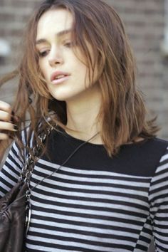 a woman with long hair is holding a cell phone and looking at the camera while wearing a black and white striped shirt