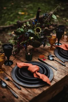 a wooden table topped with black plates and silverware next to a vase filled with flowers