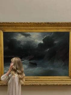 a woman standing in front of a painting talking on a cell phone while looking at it